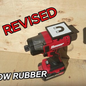 May include: A red and black cordless impact driver with a magnetic bit holder. The bit holder is labeled "REVISED" and has a magnet icon. The driver is labeled "Bauer".