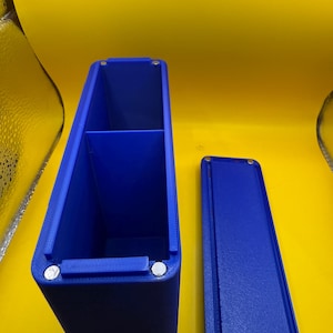 May include: A rectangular blue storage container with a divided interior and a matching detachable lid. The container features small circular silver magnets embedded at the corners of the opening and the underside of the lid for secure closure.