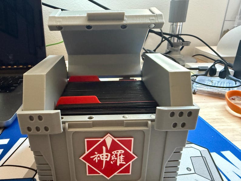May include: A gray plastic storage box with a hinged lid. The box is open and contains a stack of black cards with red dividers. The box has a red and white logo with the text "神護" on the front.