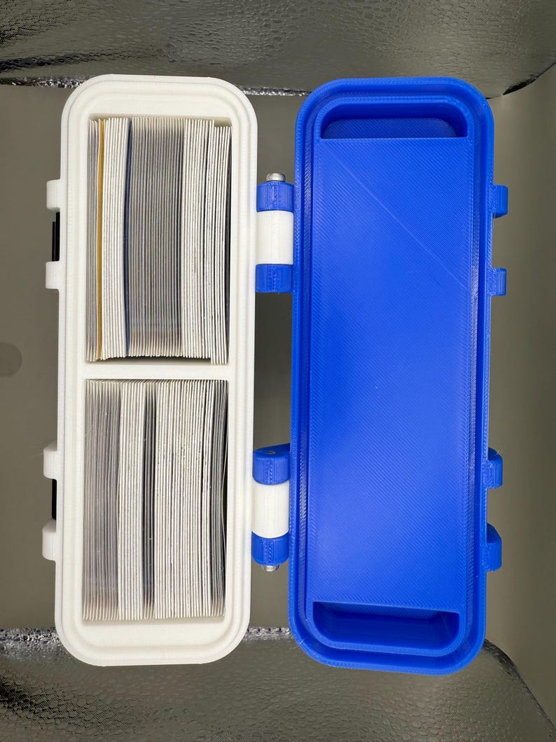 May include: A white plastic case with two compartments, one for storing cards and the other empty. The case is hinged and has a blue plastic lid.