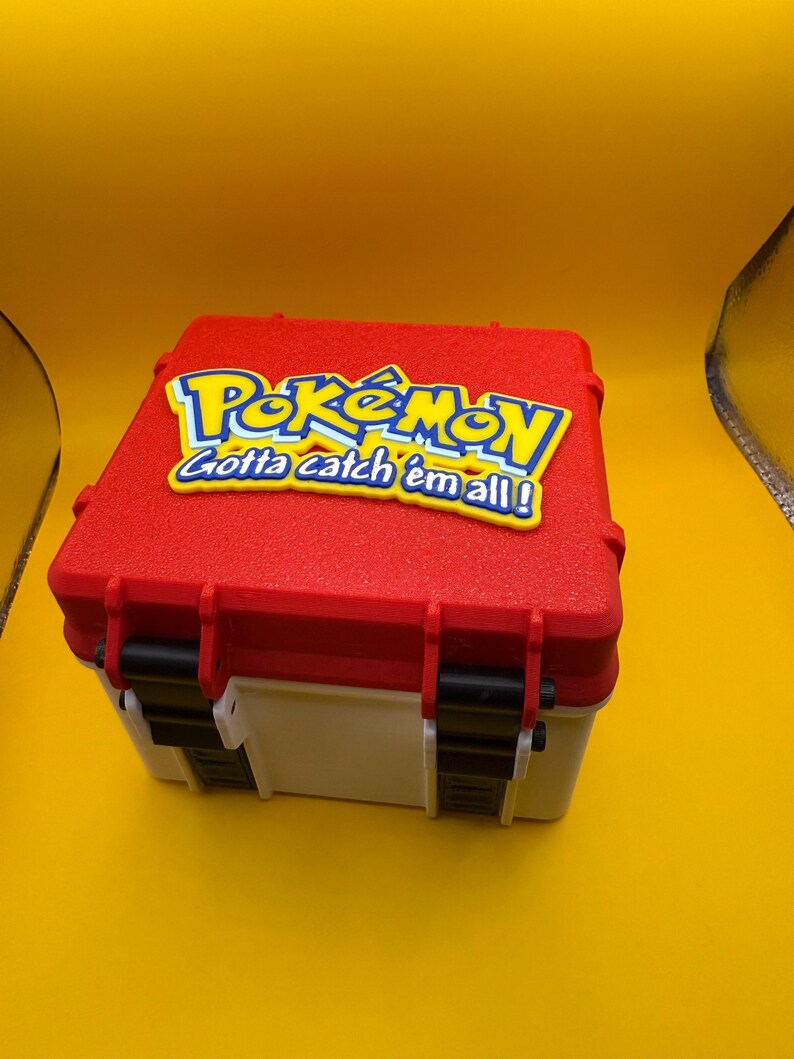 May include: A red and white plastic storage box with a black latch. The lid has a yellow Pokemon logo with the text "Gotta catch 'em all!" in blue.