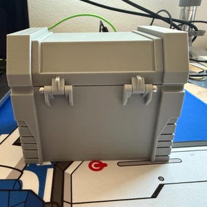 May include: A gray plastic storage box with two hinges and a latch. The box has a textured surface and is closed.