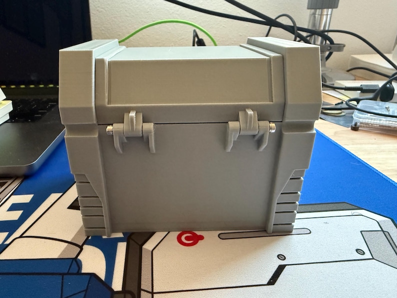 May include: A gray plastic storage box with two hinges and a latch. The box has a textured surface and is closed.