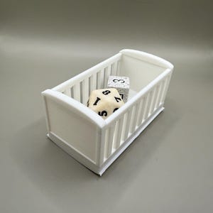 May include: A white crib-shaped container with a white and black dice inside.
