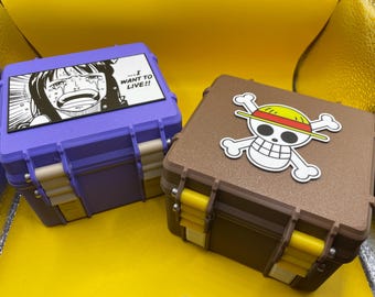 May include: Two square storage cases with latches. The purple case features a black and white manga panel of a crying character with the text "I WANT TO LIVE!!". The brown case features a white skull and crossbones logo with a straw hat.