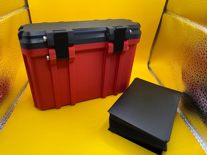 May include: A red and black plastic storage case with a stack of black card sleeves. The case has a textured lid and two latches.
