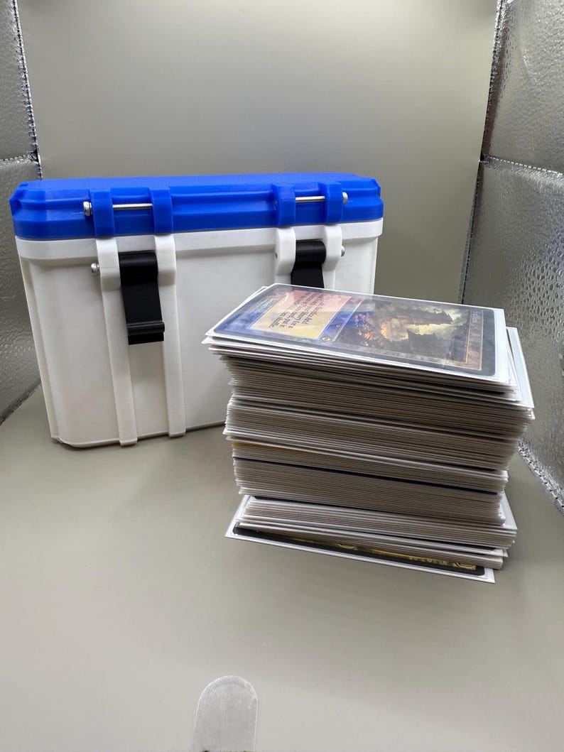 May include: A white and blue storage container with a black latch and a stack of white trading cards.