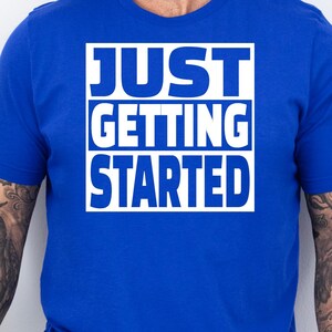 May include: A royal blue t-shirt with a white box containing the text "JUST GETTING STARTED" in all caps.