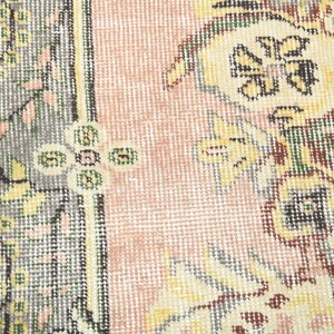 K&ouml;nnte beinhalten: Nahaufnahme eines rosa und cremefarbenen Teppichs mit Blumenmuster. Der Teppich hat einen Rand mit einem sich wiederholenden Muster aus Gr&uuml;n, Braun und Wei&szlig;.