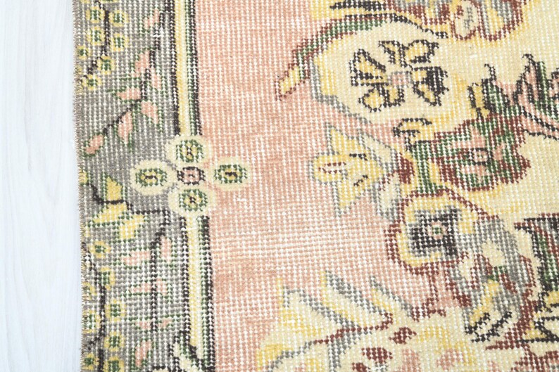 K&ouml;nnte beinhalten: Nahaufnahme eines rosa und cremefarbenen Teppichs mit Blumenmuster. Der Teppich hat einen Rand mit einem sich wiederholenden Muster aus Gr&uuml;n, Braun und Wei&szlig;.