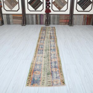 May include: A long, narrow, multi-colored rug with a faded, vintage look. The rug has a light background with shades of blue, green, orange, and red woven into the design.