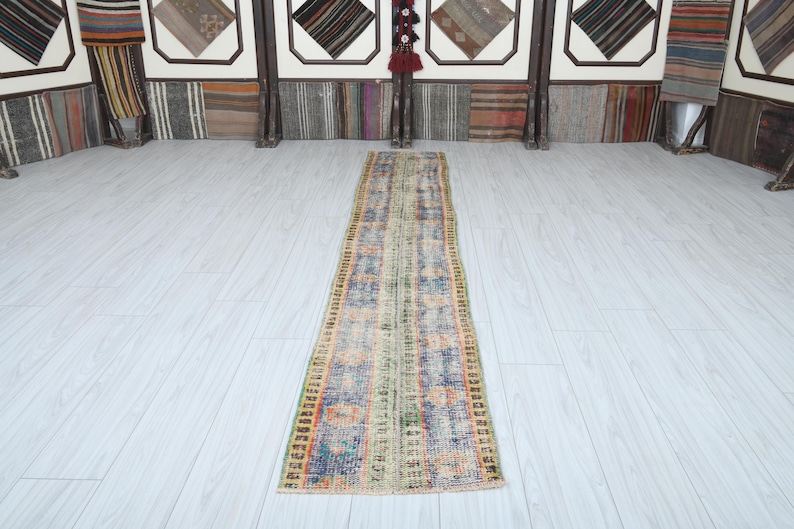May include: A long, narrow, multi-colored rug with a faded, vintage look. The rug has a light background with shades of blue, green, orange, and red woven into the design.
