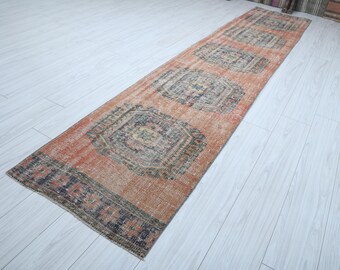 May include: A long, rectangular rug with a faded, vintage look. The rug has a light orange background with a repeating pattern of dark blue and green floral motifs. The rug is perfect for adding a touch of bohemian style to any room.