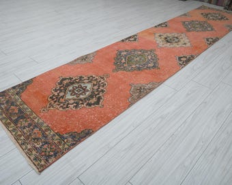 May include: A long, rectangular rug with a faded orange background and intricate floral patterns in shades of brown, green, and cream. The rug has a fringed border.