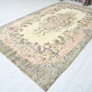 K&ouml;nnte beinhalten: Ein Vintage-Teppich mit einem floralen Muster in Rosa-, Creme- und Graut&ouml;nen. Der Teppich hat einen abgenutzten Look und ein verblichenes Aussehen.