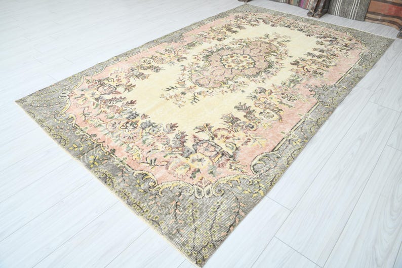 K&ouml;nnte beinhalten: Ein Vintage-Teppich mit einem floralen Muster in Rosa-, Creme- und Graut&ouml;nen. Der Teppich hat einen abgenutzten Look und ein verblichenes Aussehen.