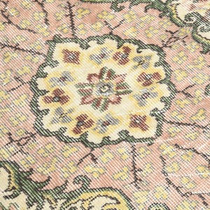 K&ouml;nnte beinhalten: Nahaufnahme eines rosafarbenen und cremefarbenen Teppichs mit Blumenmuster. Der Teppich hat ein detailliertes, kompliziertes Muster mit einem zentralen Medaillon.