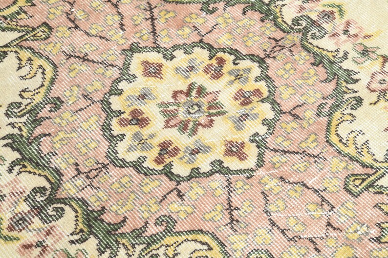 K&ouml;nnte beinhalten: Nahaufnahme eines rosafarbenen und cremefarbenen Teppichs mit Blumenmuster. Der Teppich hat ein detailliertes, kompliziertes Muster mit einem zentralen Medaillon.