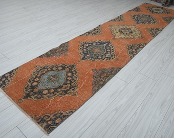 May include: A long, narrow runner rug with a traditional Persian design. The rug has a rust orange background with intricate blue, green, and black patterns.