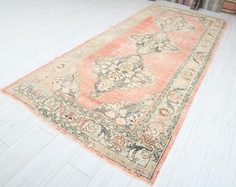 May include: A vintage rug with a peach background and intricate floral patterns in shades of beige, brown, and green. The rug has a faded, distressed look, giving it a unique and antique feel.