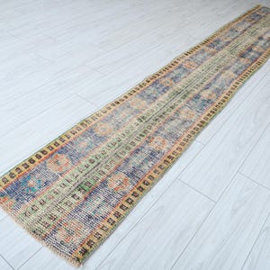 May include: A long, rectangular rug with a colorful, geometric pattern. The rug has a faded, vintage look and is made of wool. It is perfect for adding a touch of bohemian style to any room.
