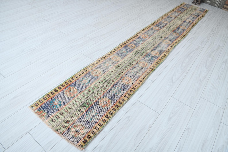 May include: A long, rectangular rug with a colorful, geometric pattern. The rug has a faded, vintage look and is made of wool. It is perfect for adding a touch of bohemian style to any room.