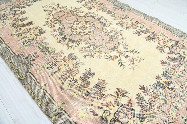 K&ouml;nnte beinhalten: Ein Vintage-Teppich mit einem floralen Muster in Rosa-, Creme- und Graut&ouml;nen. Der Teppich hat ein zentrales Medaillon mit einem sich wiederholenden floralen Design.
