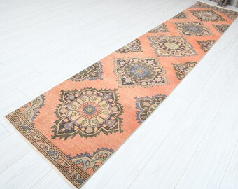 May include: A long, peach-colored runner rug with a traditional floral pattern in shades of blue, green, and brown. The rug has a fringed edge.