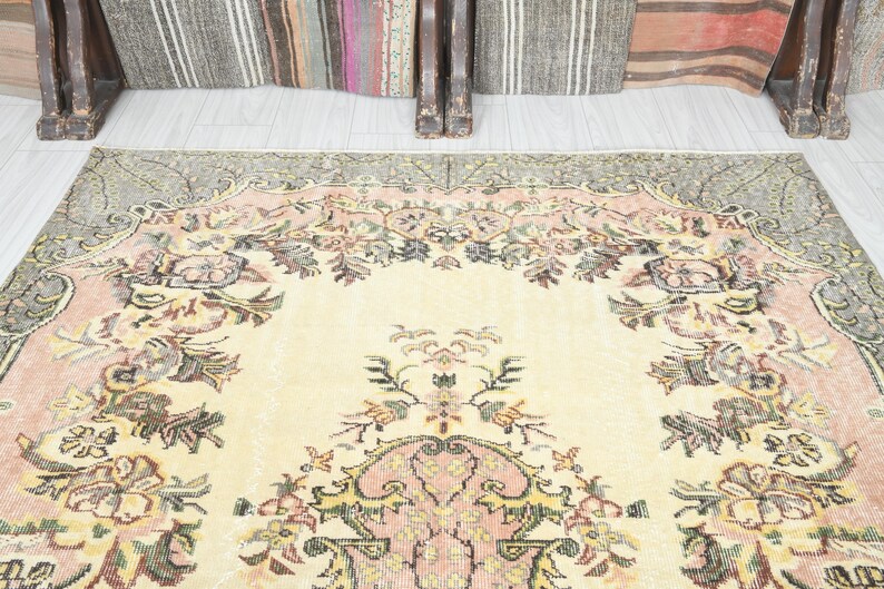 K&ouml;nnte beinhalten: Ein Vintage-Teppich mit cremefarbenem Hintergrund und einem floralen Muster in Rosa-, Gr&uuml;n- und Braunt&ouml;nen. Der Teppich hat einen verblassten, abgenutzten Look, der ihm einen einzigartigen und charmanten Charakter verleiht.