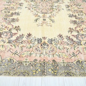 K&ouml;nnte beinhalten: Ein Vintage-Teppich mit einem floralen Muster in Rosa-, Creme- und Braunt&ouml;nen. Der Teppich hat einen abgenutzten Look und eine verblasste Optik.
