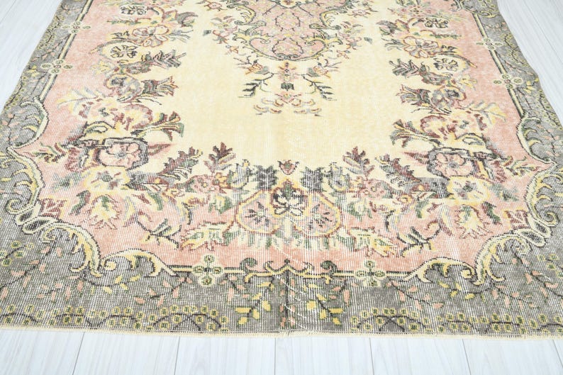 K&ouml;nnte beinhalten: Ein Vintage-Teppich mit einem floralen Muster in Rosa-, Creme- und Braunt&ouml;nen. Der Teppich hat einen abgenutzten Look und eine verblasste Optik.