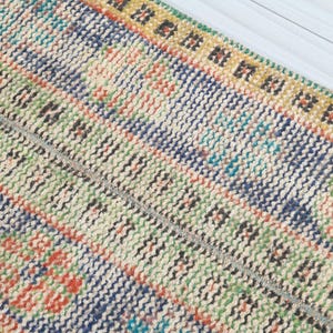May include: Close-up of a colorful woven rug with a geometric pattern. The rug has a cream background with stripes of blue, green, orange, and yellow.