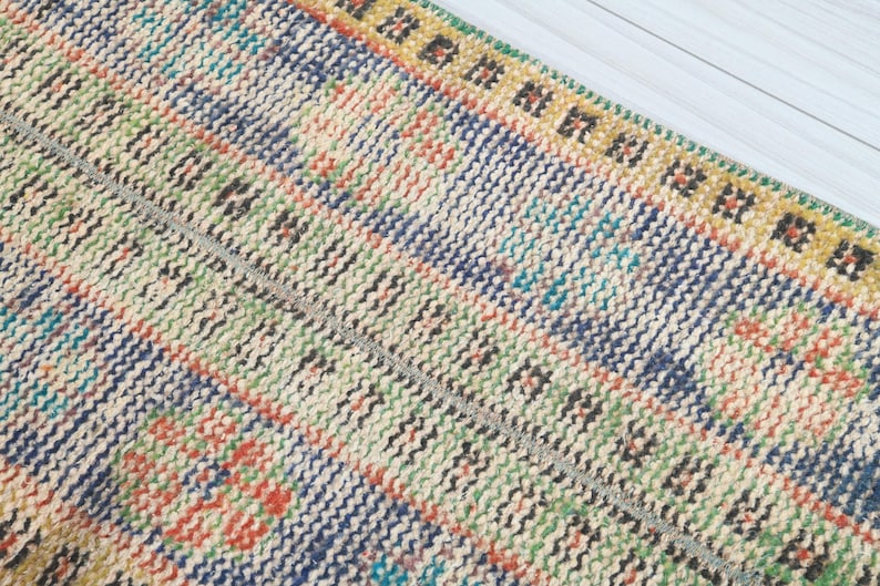 May include: Close-up of a colorful woven rug with a geometric pattern. The rug has a cream background with stripes of blue, green, orange, and yellow.