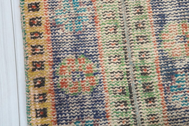 May include: Close-up of a colorful woven rug with a yellow border. The rug has a geometric pattern with blue, green, red, and white colors.