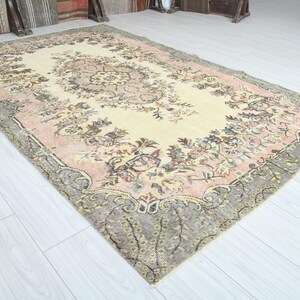 K&ouml;nnte beinhalten: Ein Vintage-Teppich mit einem floralen Muster in Rosa-, Creme- und Graut&ouml;nen. Der Teppich hat einen abgenutzten Look und ein verblichenes Aussehen.