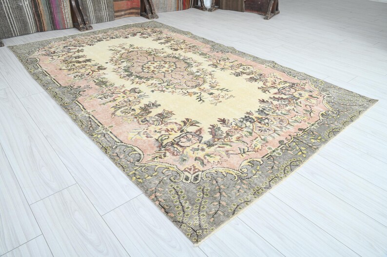 K&ouml;nnte beinhalten: Ein Vintage-Teppich mit einem floralen Muster in Rosa-, Creme- und Graut&ouml;nen. Der Teppich hat einen abgenutzten Look und ein verblichenes Aussehen.
