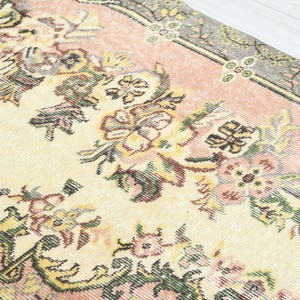 K&ouml;nnte beinhalten: Ein Vintage-Teppich mit cremefarbenem Hintergrund und rosa Rand. Der Teppich zeigt ein Blumenmuster mit filigranen Details in Gr&uuml;n-, Gelb- und Rosat&ouml;nen.