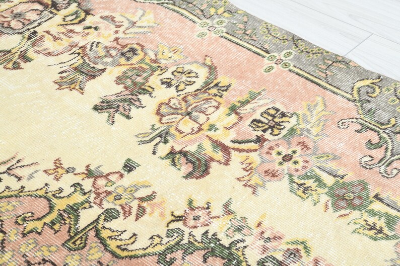 K&ouml;nnte beinhalten: Ein Vintage-Teppich mit cremefarbenem Hintergrund und rosa Rand. Der Teppich zeigt ein Blumenmuster mit filigranen Details in Gr&uuml;n-, Gelb- und Rosat&ouml;nen.