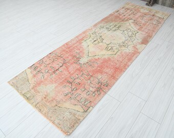 Op de afbeelding: Een rechthoekig, versleten tapijt met een vervaagde, vintage uitstraling. Het tapijt heeft een centraal medaillonontwerp in crème en olijfgroen, tegen een zalmkleurig veld. De randen van het tapijt zijn gerafeld.