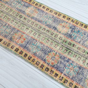 May include: A colorful patterned runner rug with a blue, green, yellow, and orange design. The rug has a fringed edge and is made of woven fabric.