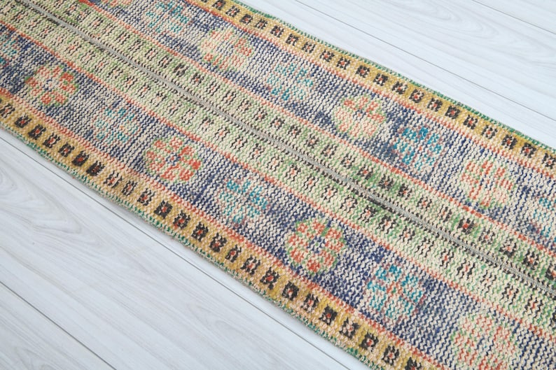 May include: A colorful patterned runner rug with a blue, green, yellow, and orange design. The rug has a fringed edge and is made of woven fabric.