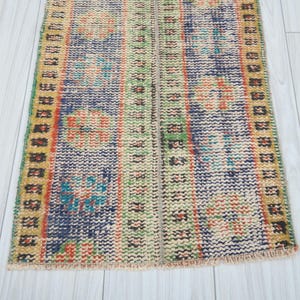 May include: A colorful vintage rug with a geometric pattern in shades of blue, green, yellow, and orange. The rug has a fringed edge and is made of wool.