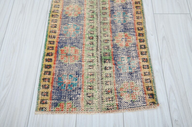 May include: A colorful vintage rug with a geometric pattern in shades of blue, green, yellow, and orange. The rug has a fringed edge and is made of wool.
