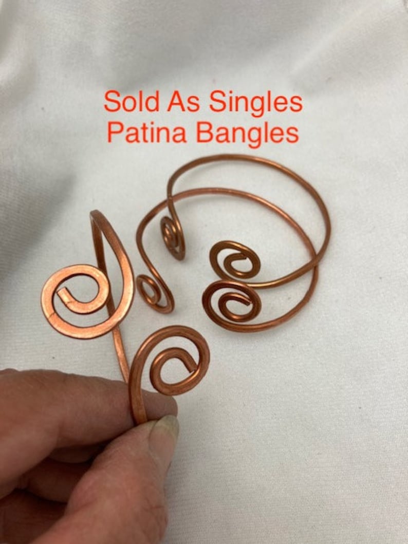 May include: Three copper wire bangles with a spiral design. The bangles are sold individually. The text "Sold As Singles Patina Bangles" is written in white text on a white background.