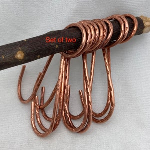 May include: Set of two hammered copper hooks. The hooks are displayed on a wooden branch.
