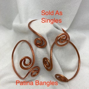 May include: Three copper wire bangles with a swirl design. The bangles are sold individually. The text "Sold As Singles" and "Patina Bangles" is visible in the image.