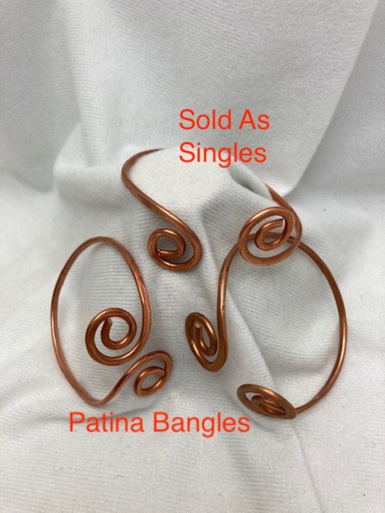 May include: Three copper wire bangles with a swirl design. The bangles are sold individually. The text "Sold As Singles" and "Patina Bangles" is visible in the image.