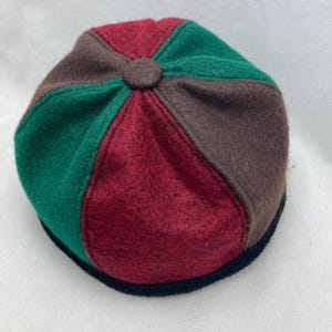 May include: A multi-colored hat with a circular design. The hat is divided into sections of red, green, and brown. A small, brown button is at the center. The hat has a black brim.