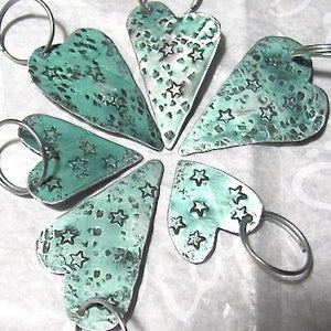May include: Six teal blue metal heart-shaped keychains with a star pattern. Each keychain has a silver ring.