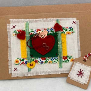 May include: Handmade card with a red felt heart, surrounded by fabric scraps in shades of green, yellow, and white. The card has a floral pattern and a small tag with a red star.